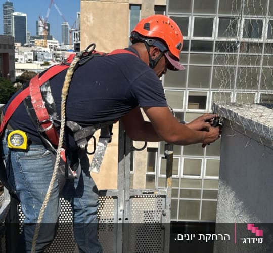 עובד מתקין רשת על גג למניעת כניסת יונים